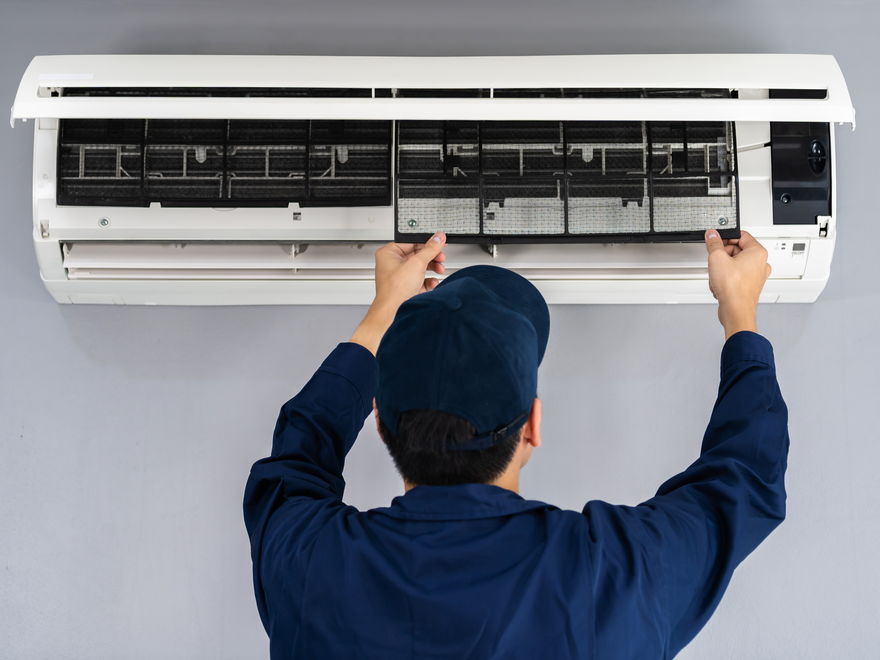 A technician in a navy uniform and cap lifting the front cover of a wall-mounted heat pump
