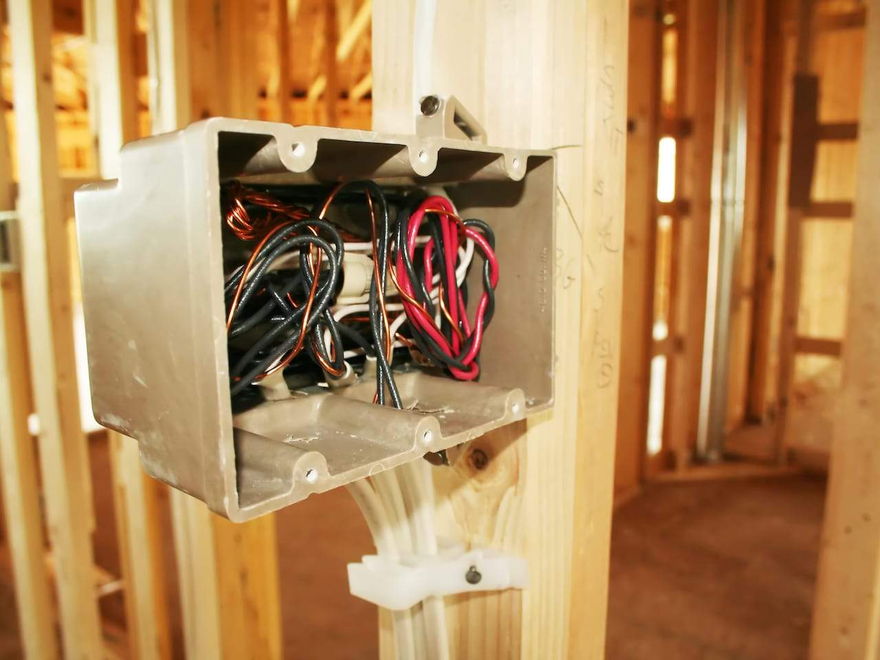 A grey flush box wired with red and black cable, fixed to the timber framing of a house under construction